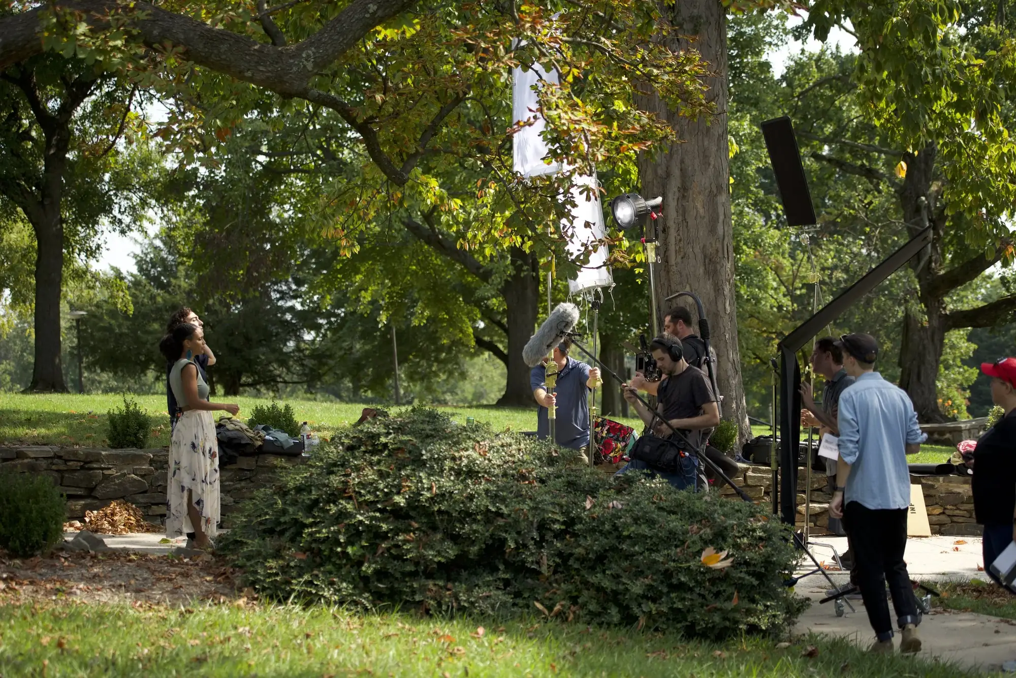 Crew filming an actor in a park under tall trees