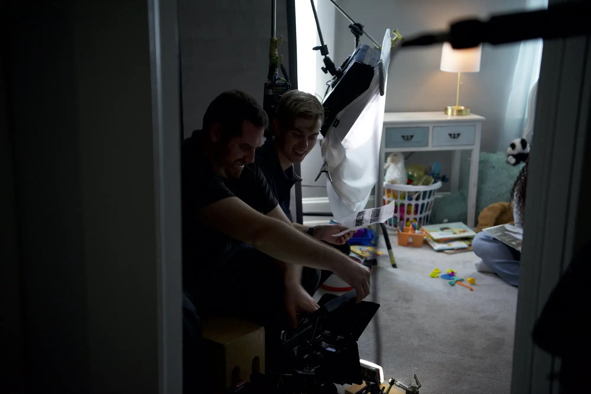 Two crew members smiling behind a camera monitor in a child's bedroom
