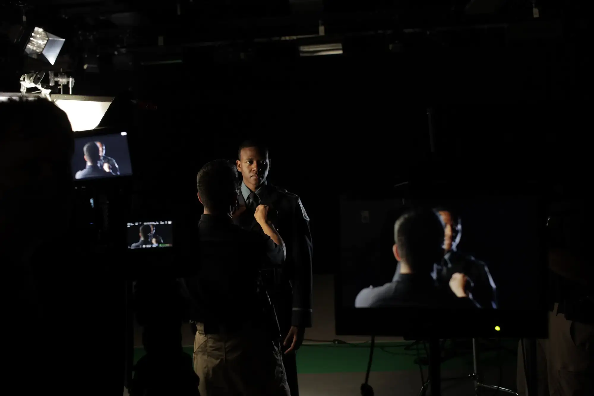 Crew filming a uniformed officer on a dark studio set