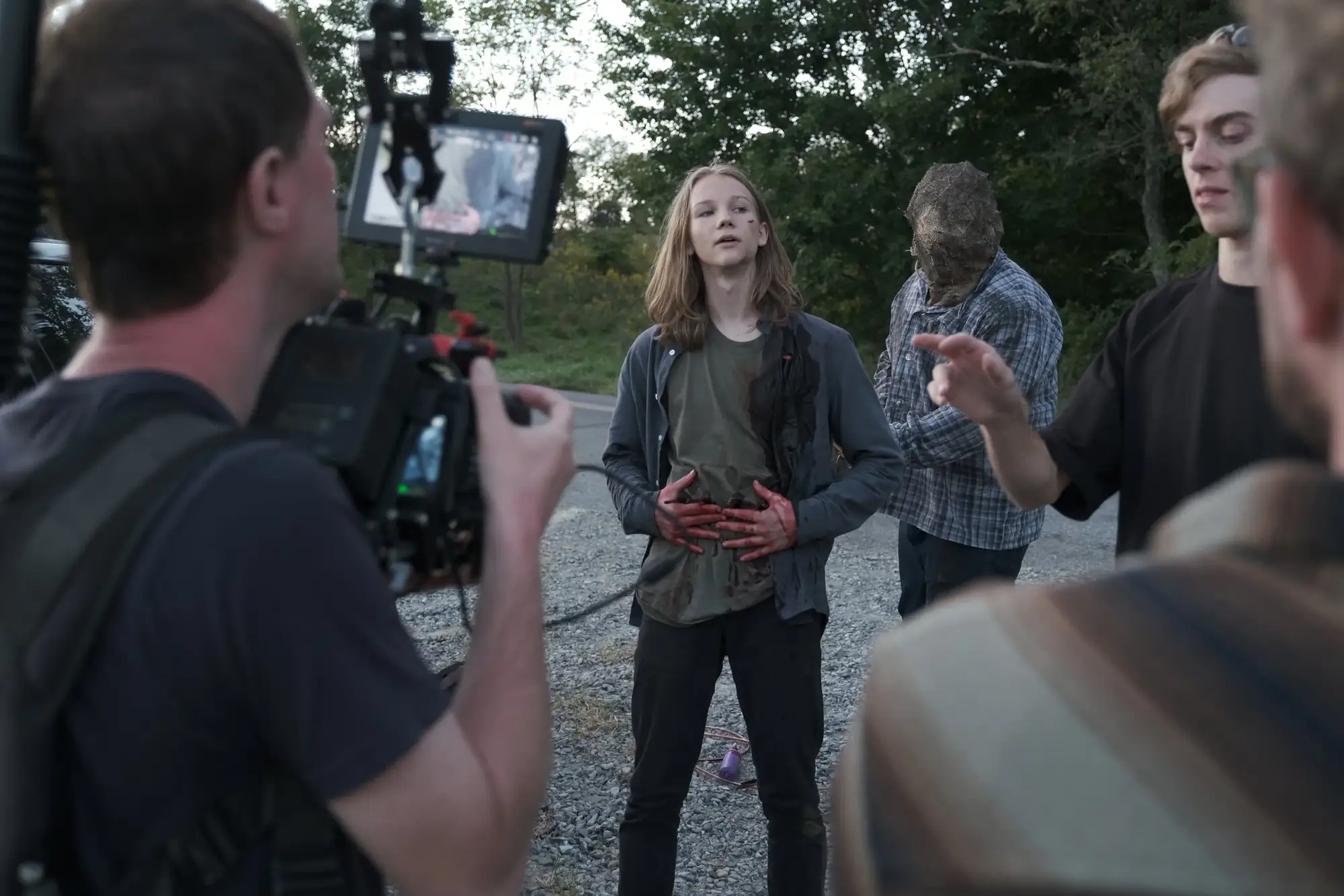 Crew filming an actor with stage blood on a gravel road