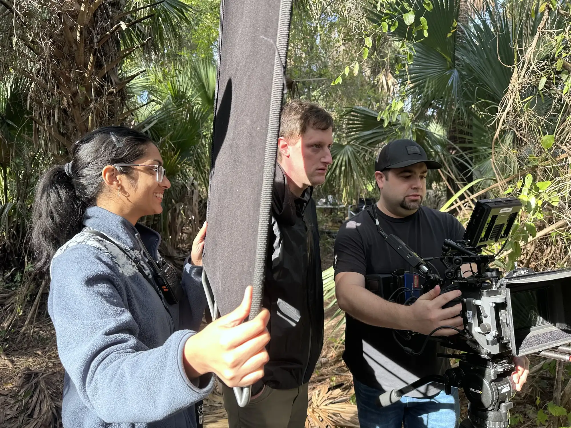 Crew holding reflector and camera rig in palmetto forest location