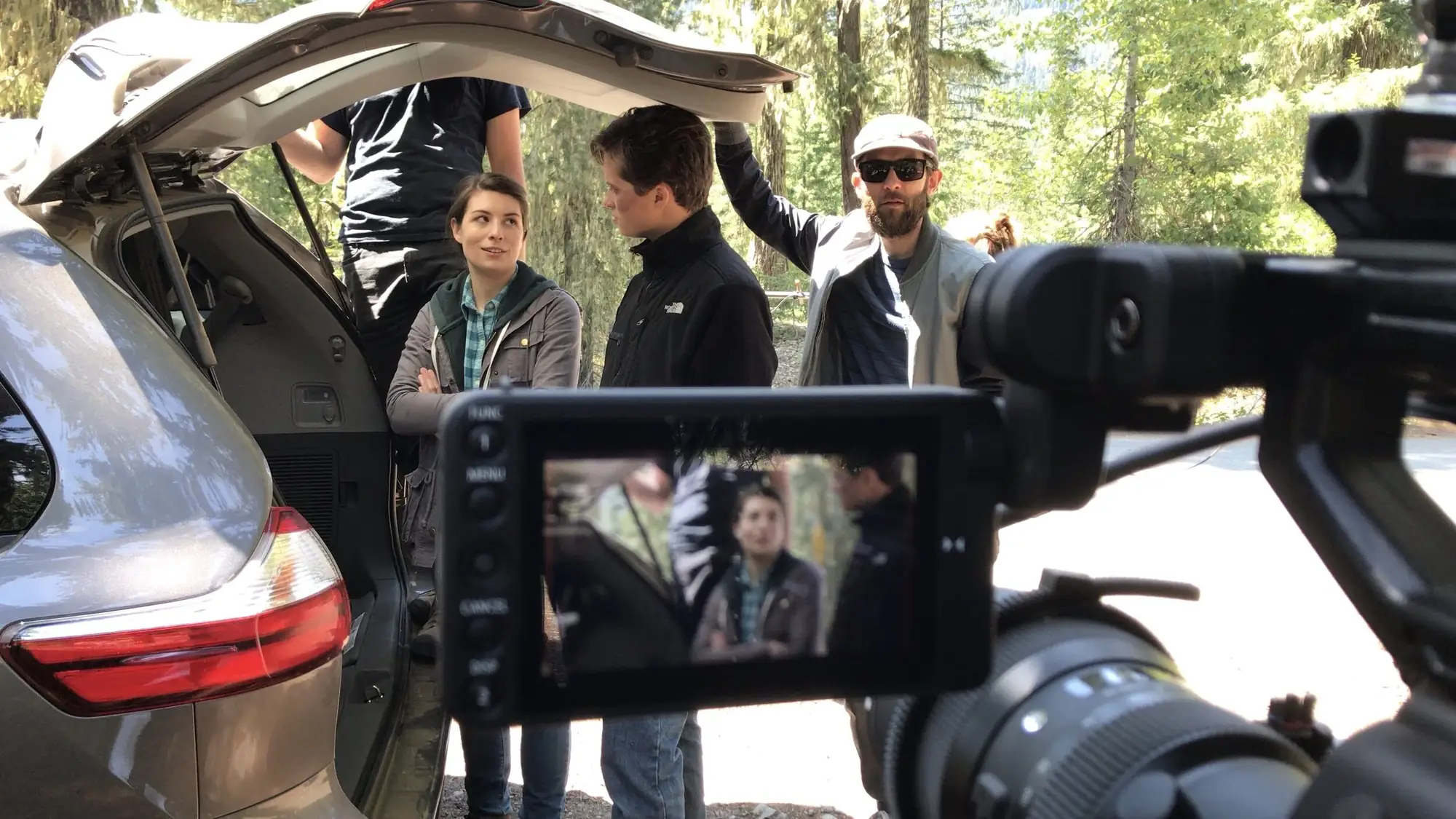 Camera monitor framing actors gathered behind an open car hatch