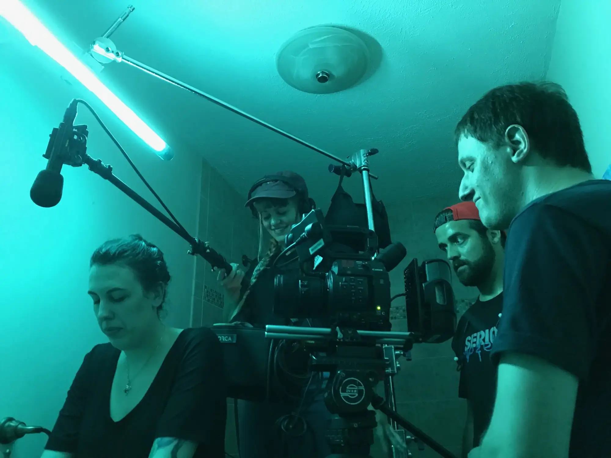 Crew filming with camera rig in a teal-lit bathroom set