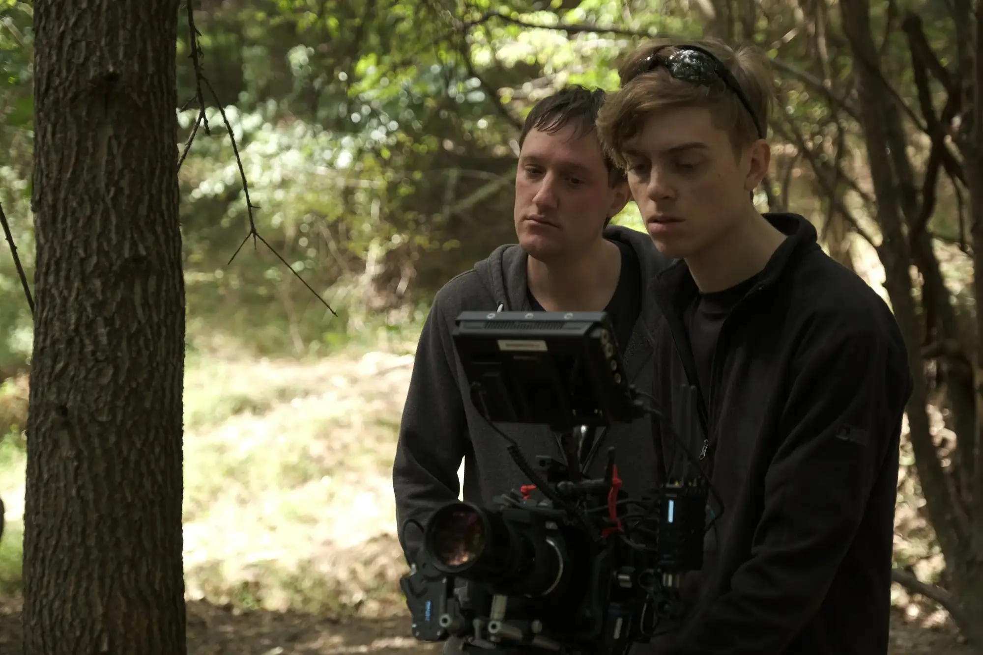 Two crew members checking a camera rig at the edge of a forest